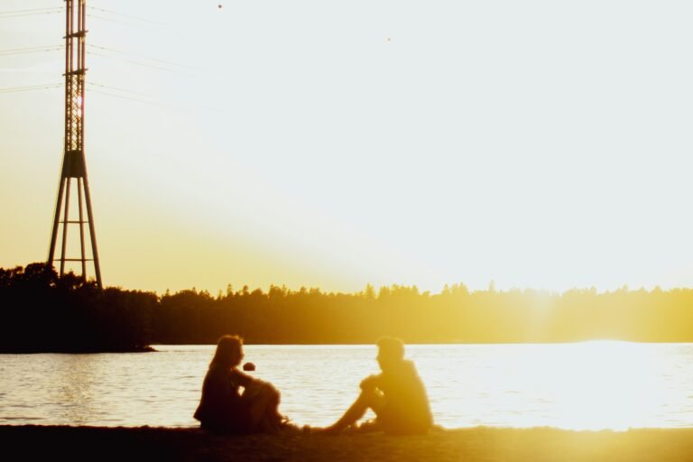 a couple of people sitting on a beach looking at a large tower