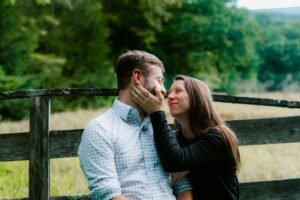 Couple embraces near a rustic wooden fence outdoors.