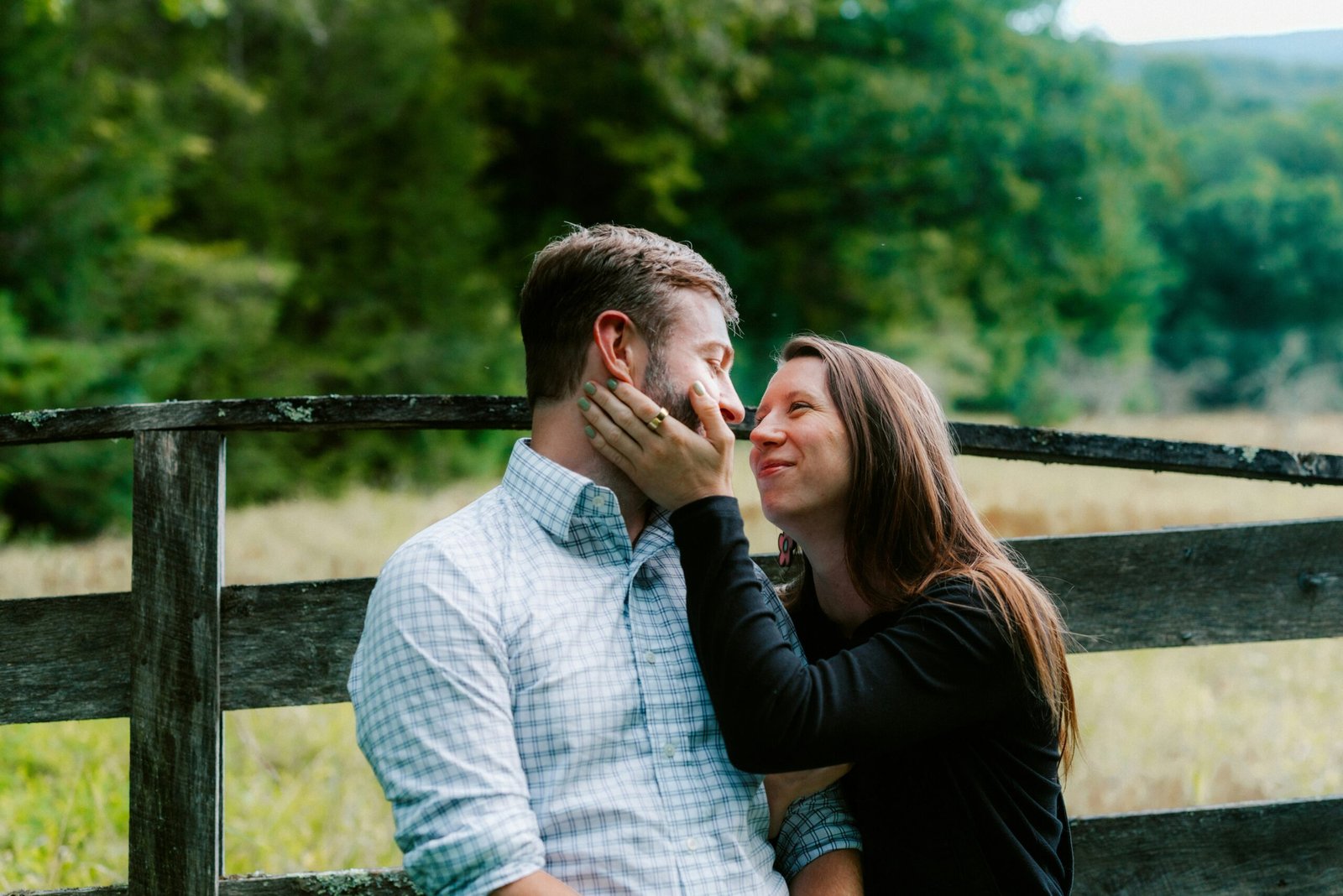 Couple embraces near a rustic wooden fence outdoors.